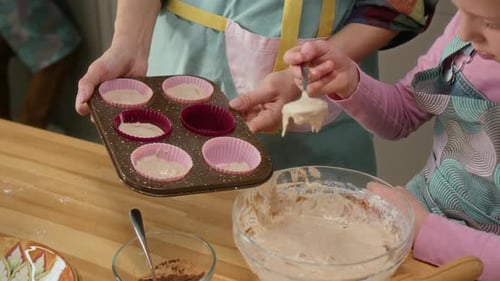 Mama und Tochter füllen Muffinblech mit Teig