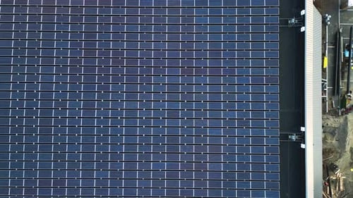 Aerial top down pan across solar panels lining industrial building supplying energy to system