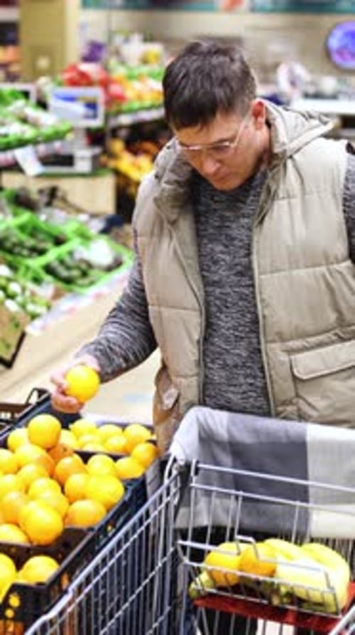 Vertical Video of a Man Picking Oranges From a Supermarket Counter and Adding Them to His Basket