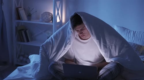 Man Works on Laptop in Bed at Night