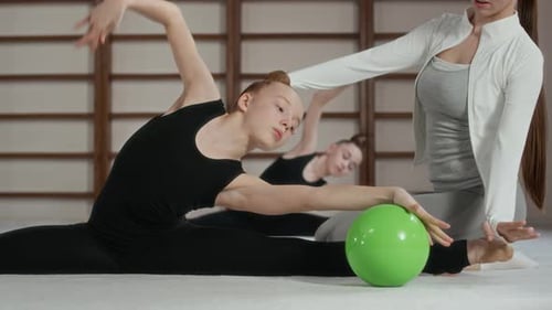 Graceful Girl in Bodysuit Side Bending and Rolling Green Ball on the Floor