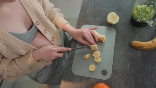 Momtobe, enceinte, hache une banane à bord pour un smoothie, bol d'avoine et de yogourt Visible Upbeat Morning
