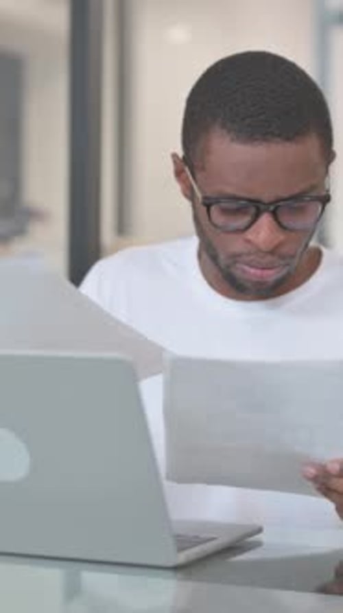 Man Reviews Paperwork While Working on Laptop