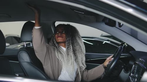 Woman Smiling While Adjusting Interior Lights in a Modern Car Inside an Indoor Parking Facility