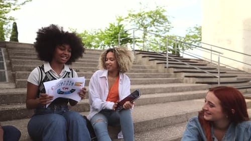 multiracial classmates on campus sitting on stairs studying and having fun.