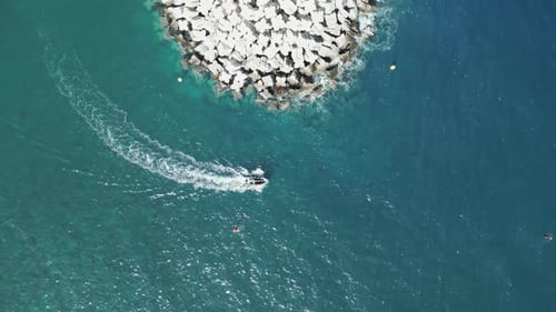 Boat exits port harbor rounding corner of large breakwater, drone top down bird's eye view static
