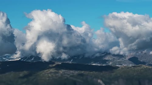 Dense clouds whirl above the vast mountainous plateau casting dark shadows on the ground. A timelaps