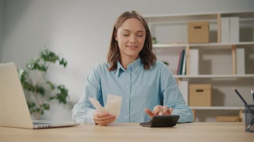 Satisfied Young Woman Accountant Use Calculator to Check Sums in Annual Report