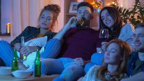 Young adults relaxing on sofa, drinking and watching TV