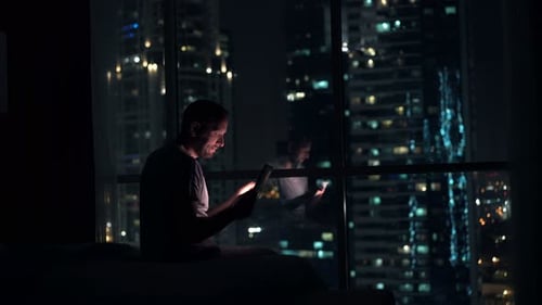 Young Man Browsing Web on Tablet Computer Sitting on Bed at Home