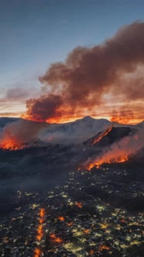 Un feu de forêt se propage à travers les montagnes au-dessus de la ville illuminée la nuit
