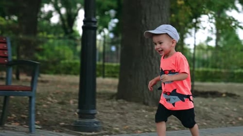 Adorável menino sorridente com boné e camiseta correndo pelo parque.