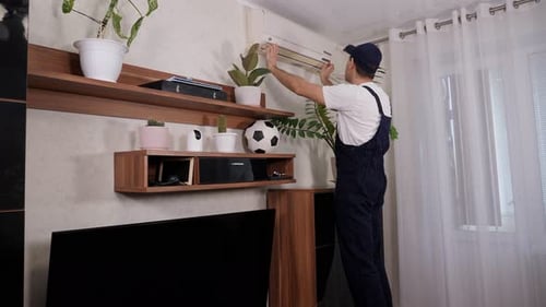 Male Handyman in Overalls Repairs or Cleans the Air Conditioner in the Apartment