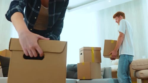 Close Up of Positive Young Man and Woman in Room with Many Boxes Putting Stuff on Floor