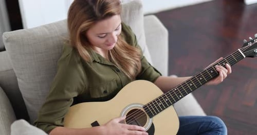 Woman Plays Acoustic Guitar While Relaxing on Sofa