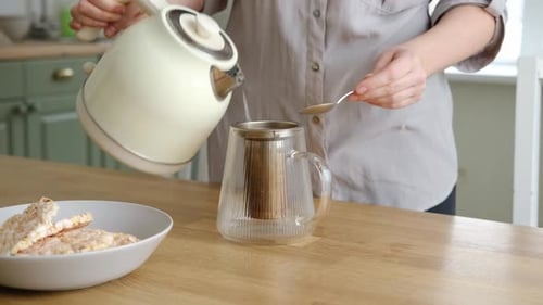 Woman Pours Hot Water into Glass Teapot