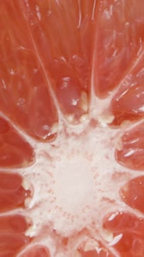 Vertical video. Top view of a slowly rotating grapefruit half, as the camera gradually zooms out fro