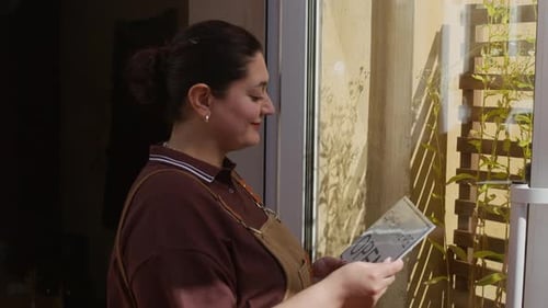 Female Worker in Apron Opening Cafe Placing Sign on Entrance Door
