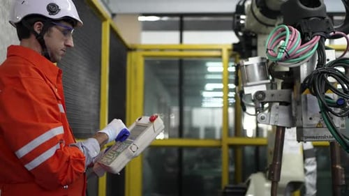 Blue collar workers at workshop with welding robot arm for automotive industry.