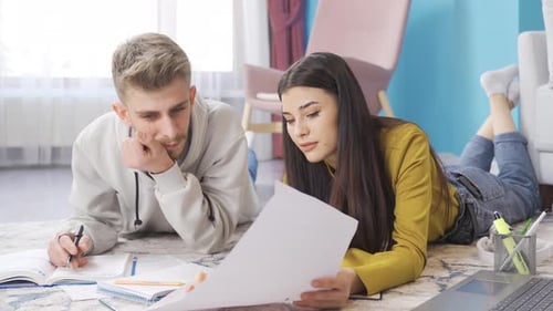 Étudiants de sexe masculin et féminin assis par terre avec leur ordinateur portable et écrivant des devoirs ou de la composition.