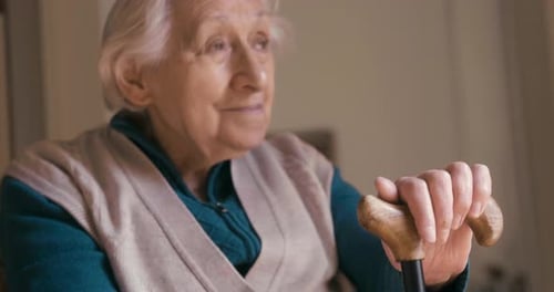 Authentic close up shot of smiling disabled senior woman with a stick is looking outside a window.