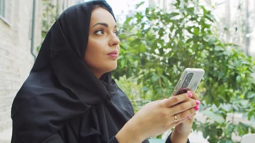 Woman with Headscarf Uses Smartphone in Urban Setting