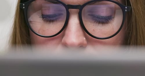 Nahaufnahme einer fokussierten Frau mit Brille, die auf den Laptop-Bildschirm schaut