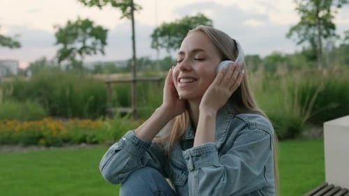 Young Woman Enjoys Listening to Music and Singing While Sitting in Park