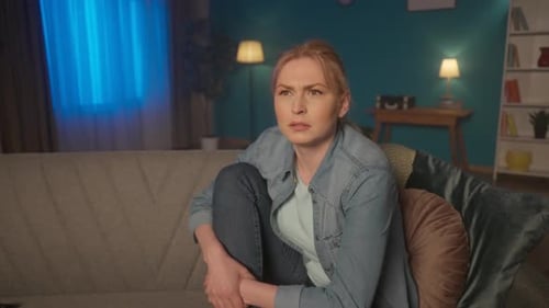 A Young Woman Sits on a Sofa with Legs and Watches TV in the Evening A Woman Watches a Movie Series