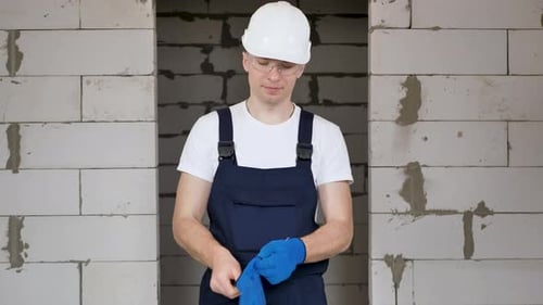 A Male Construction Worker in a Protective Helmet and Glasses Wears Blue Gloves
