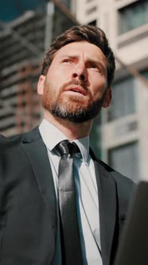 Bearded Man Works on Laptop Sitting Near Office Building