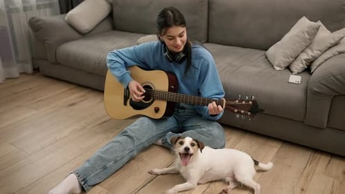 Woman Plays Guitar with Dog at her Feet