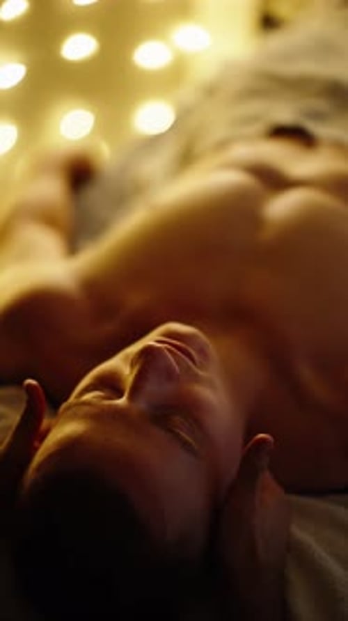 Gros plan serein d'un homme couché recevant un doux massage des tempes baigné dans un bokeh doré chaud