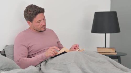 Man Reading a Book in Bed Indoors