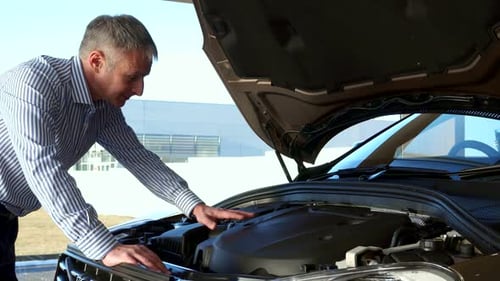 Mature Man Inspects Car Engine at Dealership