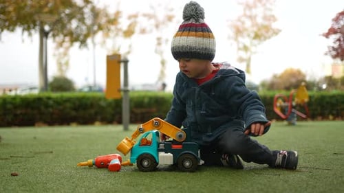 Little boy playing with truck outside at park during autumn day. Child wearing beanie and jacket