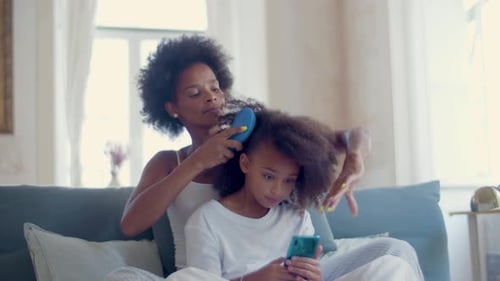 Woman Brushing Child's Hair on Couch Indoors