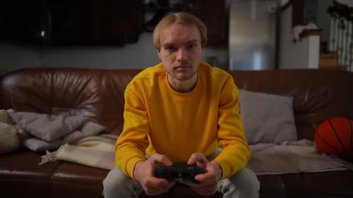 Front View Portrait of Blond Adult Man Sitting on Couch Playing Video Game with Joystick Medium Shot