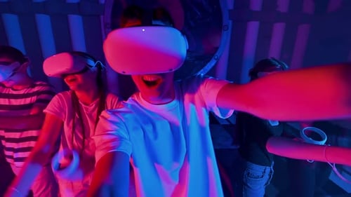 A team of young friends play virtual reality games in VR equipment on an arena. Neon lights