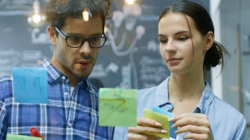 Colleagues Brainstorming Together Using Sticky Notes on Glass