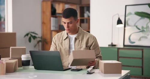 Young Man Packing Boxes at Desk with Laptop