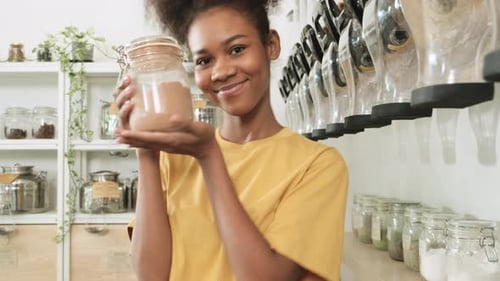 A young woman shops in refill store with reusable and zero-waste containers.