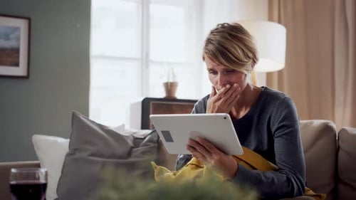 Distraught woman looking at tablet on the sofa