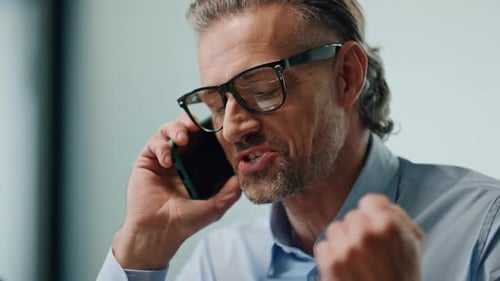 Happy director rejoicing at smartphone conversation in modern office