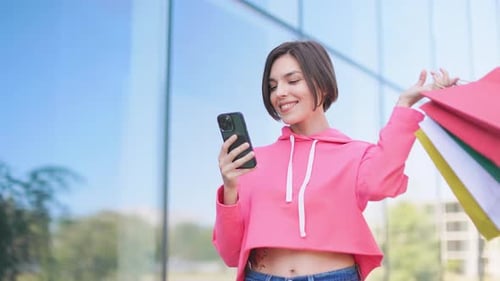 Woman Using Phone Holding Shopping Bags Outside