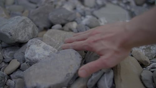 Person Touching and Feeling Stones Rocks Outdoors in Riverbed