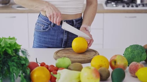 Mujer con cuchillo afilado cortando la naranja en dos mitades.