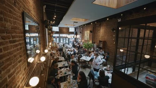 High Angle of a Bustling Restaurant Interior with Brick Walls Where Customers Eat Nd Waiters Serve