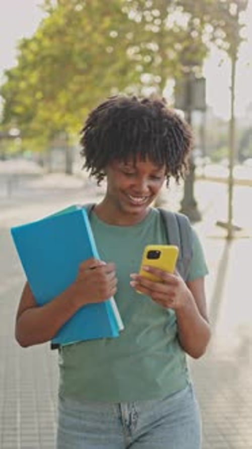 Happy Woman Walks Down Urban Sidewalk with Phone
