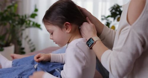 Woman Combs Little Girl's Long Brown Hair Indoors